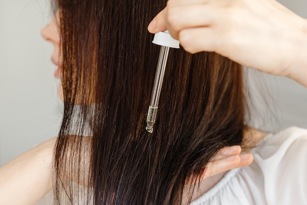 Concept de soins capillaires Femme appliquant un compte-gouttes avec de l'essence d'huile ou de sérum sur les pointes des cheveux Gros plan