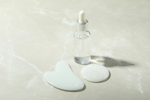 Concept de soins du visage avec gua sha et cosmétique sur fond texturé clair