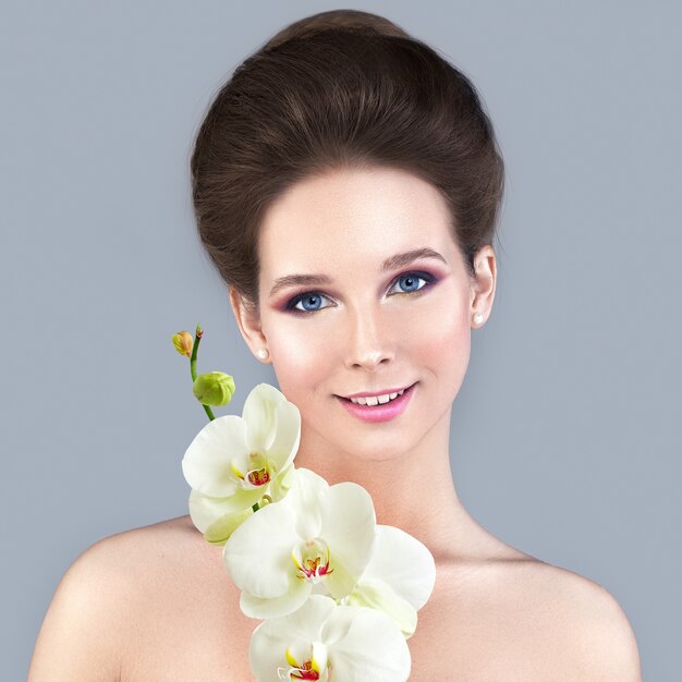Concept De Soins De La Peau De Spa. Femme en bonne santé avec une peau claire et une fleur d'orchidée blanche