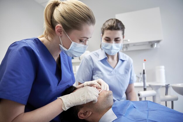concept de soins des personnes, de la médecine, de la stomatologie et des dents - femme dentiste avec assistant vérifiant les dents d'occlusion dentaire du patient masculin au bureau de la clinique dentaire