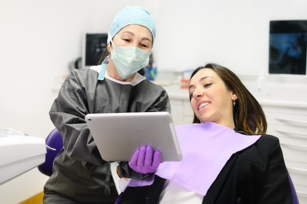 Concept de soins de santé - femme dentiste montrant une tablette tactile à une patiente au bureau de la clinique dentaire.