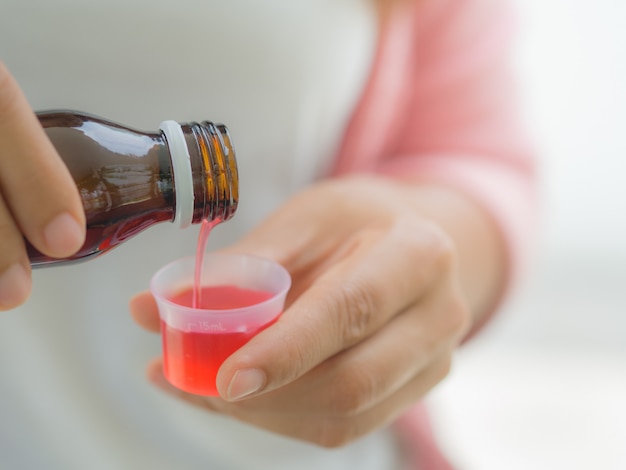 Concept de soins de santé - femme verser un sirop antipyrétique de bouteille à tasse