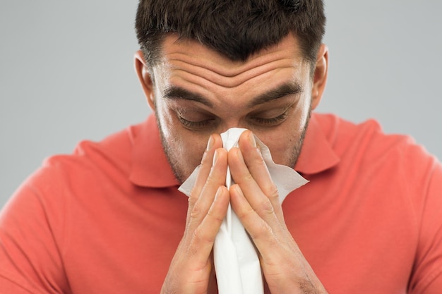 concept de soins de santé, grippe, allergie, hygiène et personnes - homme malade se mouchant le nez à la serviette en papier à la maison