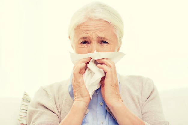 concept de soins de santé, de grippe, d'hygiène, d'âge et de personnes - femme âgée malade se mouchant le nez à la serviette en papier à la maison