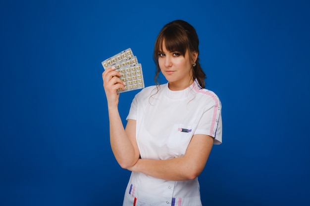 Le concept de soins de santé. Une jeune médecin brune en blouse blanche sur fond bleu montre des assiettes avec des capsules à prendre.