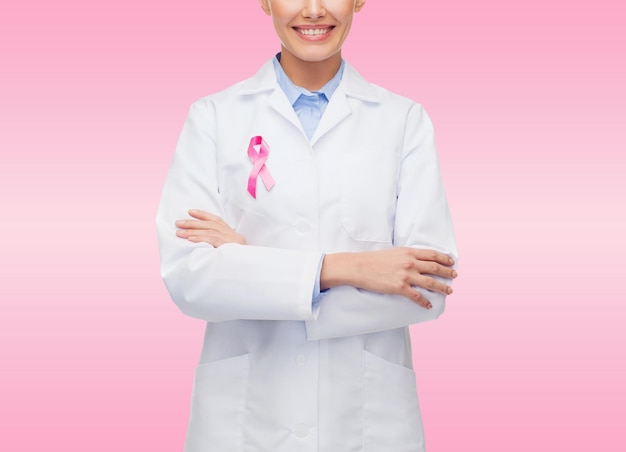 concept de soins de santé et de médecine - gros plan d'une femme médecin souriante avec un ruban rose de sensibilisation au cancer sur fond rose