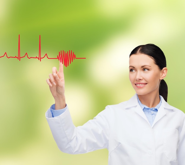 Photo concept de soins de santé, de médecine et de technologie - femme médecin souriante pointant vers le cœur et le cardiogramme