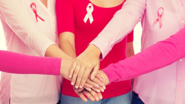concept de soins de santé, de personnes, de gestes et de médecine - gros plan de femmes en chemises vierges avec des rubans roses de sensibilisation au cancer du sein mettant les mains sur le dessus sur fond blanc