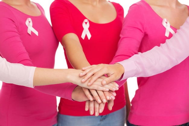Photo concept de soins de santé, de personnes, de gestes et de médecine - gros plan de femmes en chemises vierges avec des rubans roses de sensibilisation au cancer du sein mettant les mains sur le dessus sur fond blanc