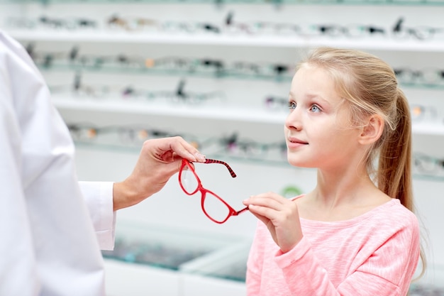 concept de soins de santé, de personnes, de vue et de vision - opticien donnant des lunettes à une petite fille dans un magasin d'optique