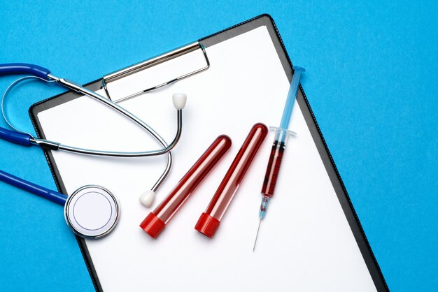 Concept de soins de santé - stéthoscope, tube à essai sanguin, seringue et presse-papiers avec feuille vierge.