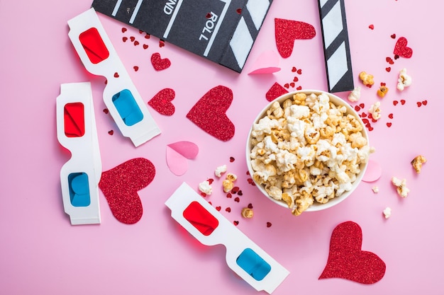 Concept de soirée cinéma de la Saint-Valentin. Pop-corn, panneau de clapet de lunettes 3d sur fond rose. Plans de vacances cosy pour les amoureux