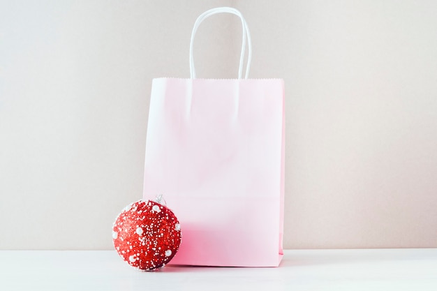 Le concept des soldes de vacances. Sur fond beige, un cabas en papier rose et un ballon de Noël rouge.