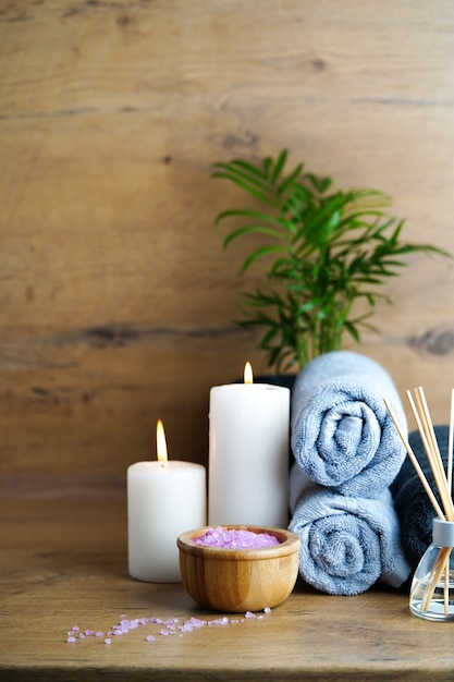 Concept de spa et d'aromathérapie-bougies, serviettes, sel de mer rose et diffuseur de roseaux aromatiques sur une table en bois.