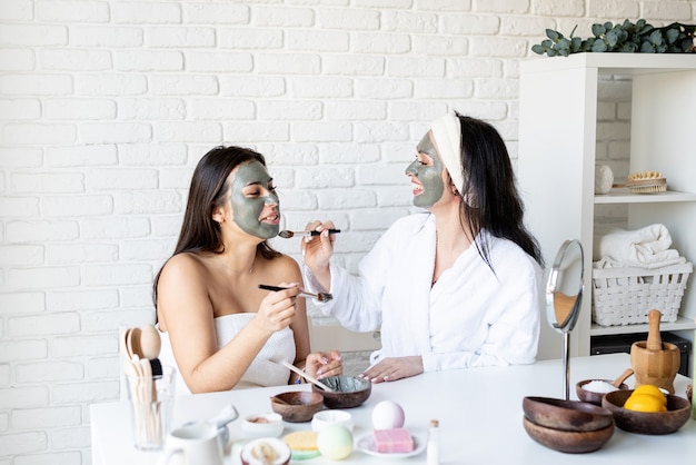 Concept de spa et de bien-être. Soins auto-administrés. deux belles femmes appliquant un masque facial s'amusant