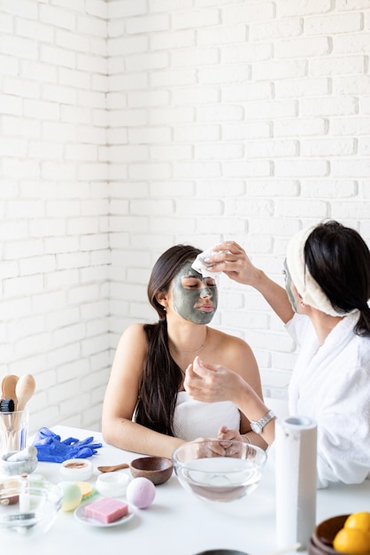 Concept de spa et de bien-être. Soins auto-administrés. Deux belles femmes en peignoirs appliquant un masque facial s'amusant