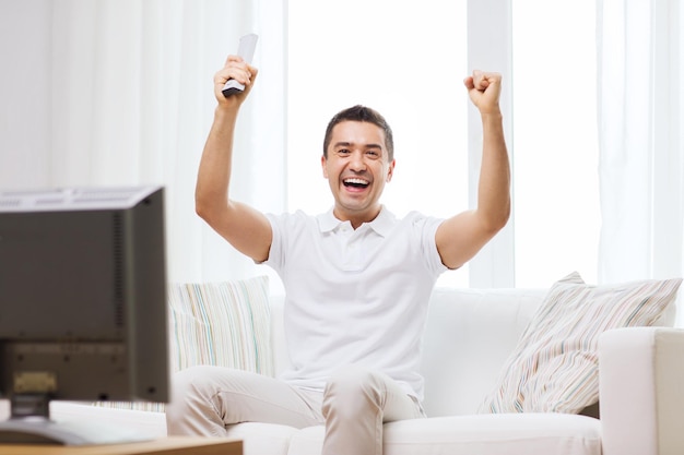 concept de sport, de bonheur et de personnes - homme souriant regardant des sports à la télévision et soutenant l'équipe à la maison