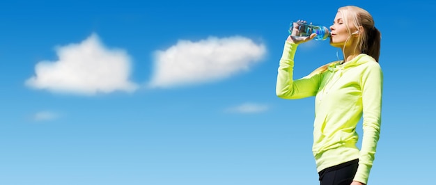 concept de sport, de fitness, d'exercice, de personnes et de style de vie - femme buvant de l'eau après avoir fait du sport à l'extérieur sur fond bleu ciel et nuages