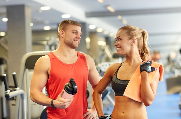 concept de sport, de fitness, de style de vie et de personnes - homme et femme souriants avec une bouteille de boisson protéinée et une serviette parlant dans la salle de sport