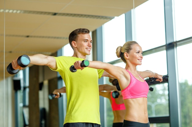concept de sport, de fitness, de style de vie et de personnes - homme et femme souriants avec des haltères faisant de l'exercice dans la salle de gym