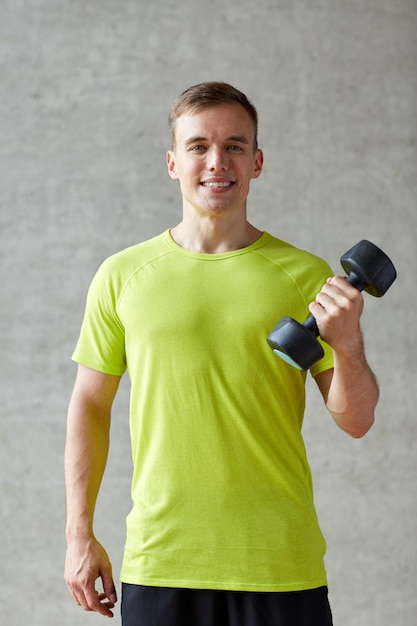 concept de sport, de fitness, de style de vie et de personnes - homme souriant avec haltère fléchissant les biceps dans la salle de sport