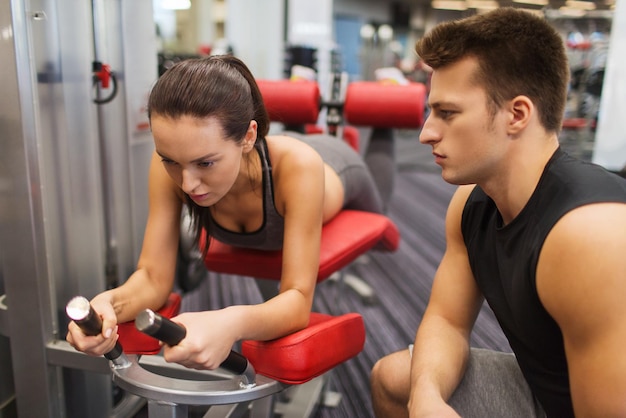 concept de sport, de fitness, de style de vie et de personnes - jeune femme et entraîneur personnel fléchissant les muscles des jambes sur une machine de gym