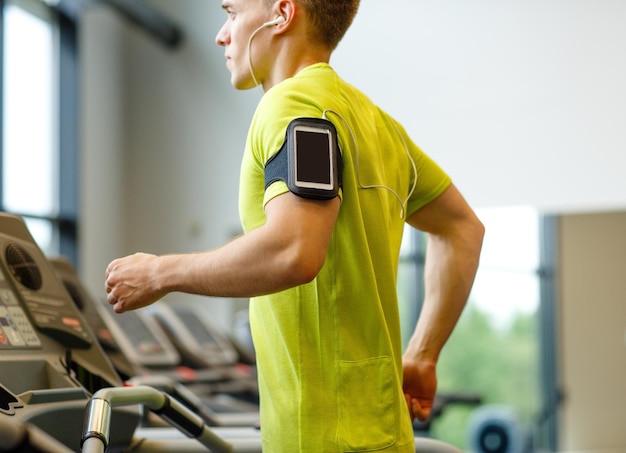 concept de sport, de fitness, de style de vie, de technologie et de personnes - homme avec smartphone et écouteurs faisant de l'exercice sur tapis roulant dans la salle de sport