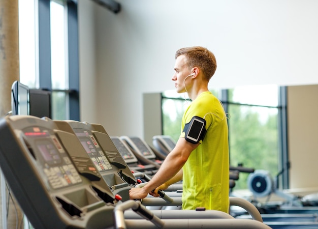 concept de sport, de fitness, de style de vie, de technologie et de personnes - homme avec smartphone et écouteurs faisant de l'exercice sur tapis roulant dans la salle de sport