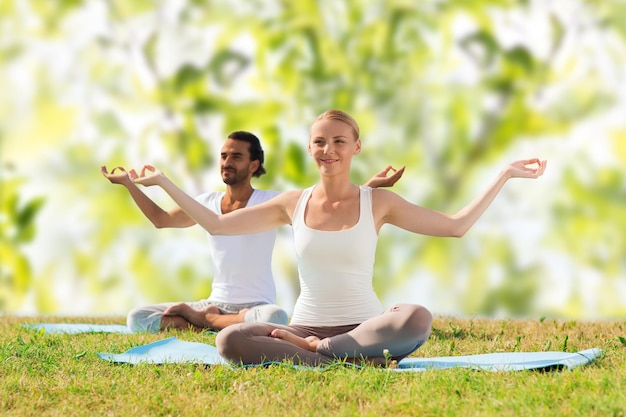 concept de sport, de fitness, de yoga et de personnes - couple souriant méditant et assis sur des tapis sur fond de feuilles d'arbres verts