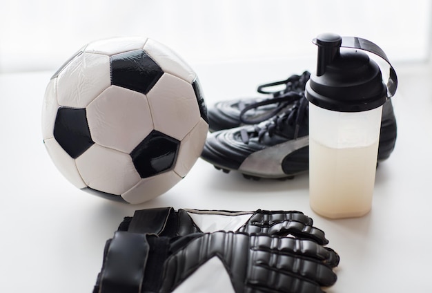 concept de sport, de football et d'équipement sportif - gros plan sur un ballon, des chaussures de football, des gants de gardien de but et une bouteille de boisson protéinée avec boisson