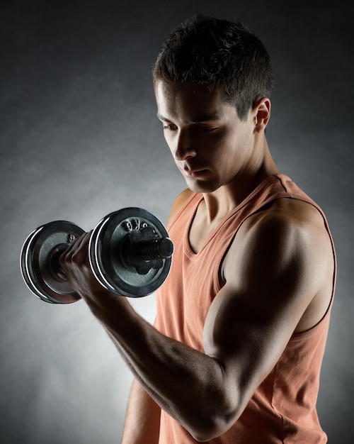 concept de sport, de musculation, d'entraînement et de personnes - jeune homme avec des muscles fléchissants d'haltères sur fond gris