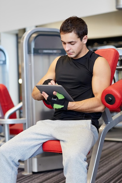 concept de sport, de musculation, de mode de vie, de technologie et de personnes - jeune homme avec un ordinateur tablette dans la salle de sport