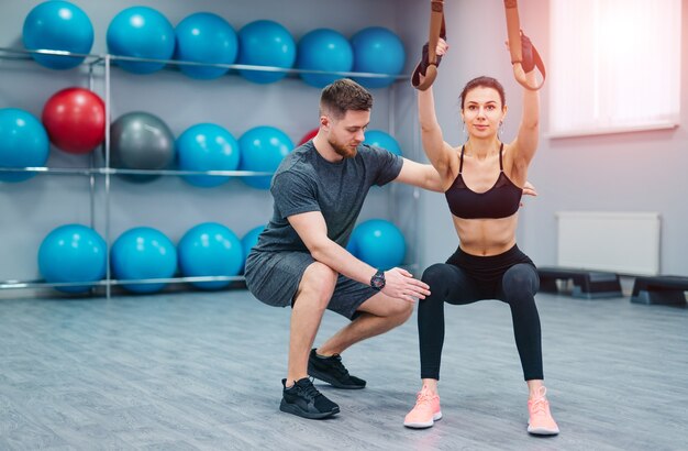 Concept de sport, de musculation, de style de vie et de personnes - jeune homme et femme s'entraînant dans une salle de sport. L'entraîneur et la fille de remise en forme s'entraînent au gymnase.