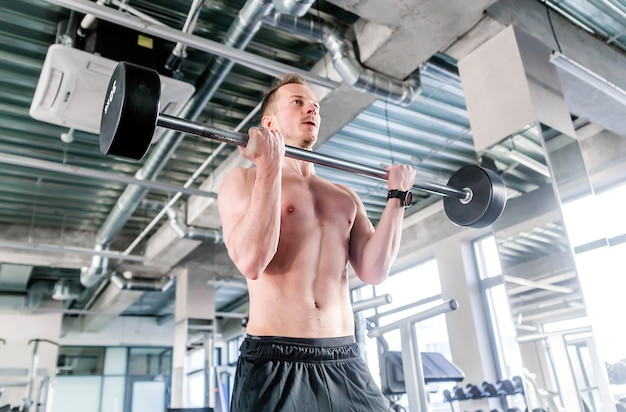 Concept de sport, de musculation, de style de vie et de personnes - jeune homme avec haltères fléchissant les muscles dans la salle de gym. photo horizontale