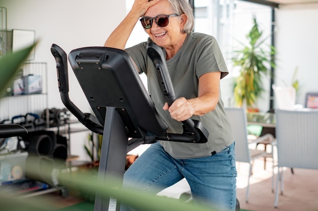 Concept de sport de personnes Femme senior souriante faisant du vélo à vélo stationnaire sur la terrasse de la maison