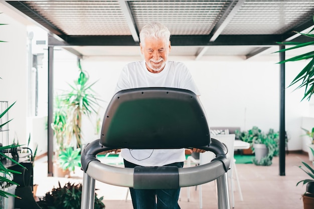 Concept de sport de personnes Heureux homme âgé faisant des exercices pour rester en forme en courant sur un tapis roulant en terrasse