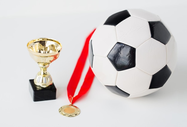 concept de sport, de réalisation, de championnat, de compétition et de réussite - gros plan d'un ballon de football ou de soccer avec médaille d'or et coupe sur fond blanc