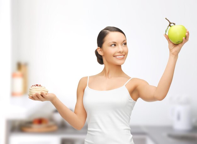 concept de sport et de régime - femme sportive avec pomme et gâteau dans la cuisine