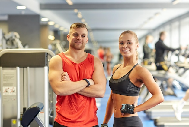 Concept de sport, de remise en forme, de style de vie et de personnes - homme et femme souriants dans la salle de gym