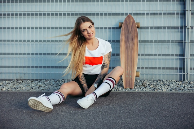 Concept de sport, de style de vie, d'extrême et de personnes - Tatouages de belles filles faisant du longboard sur la route de la ville par temps ensoleillé. Portrait hipster girl smiling avec un longboard au coucher du soleil.