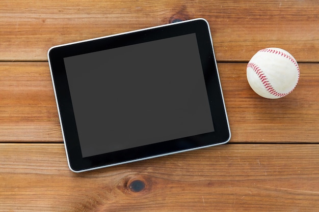 concept de sport, de technologie, de jeu et d'objets - gros plan d'une balle de baseball et d'un ordinateur tablette sur parquet