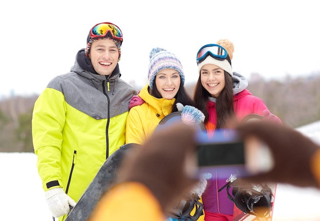 concept de sports d'hiver, de loisirs, d'amitié, de technologie et de personnes - amis heureux avec des snowboards et un smartphone prenant des photos