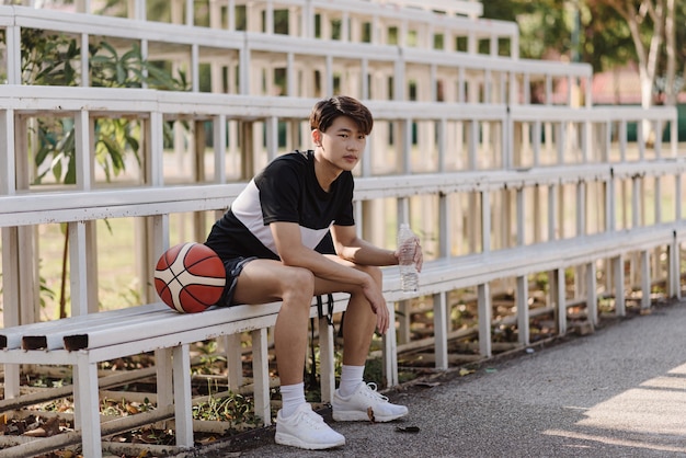 Concept de sports et de loisirs un jeune joueur de basket-ball assis sur une tribune à la frontière du terrain de sport.