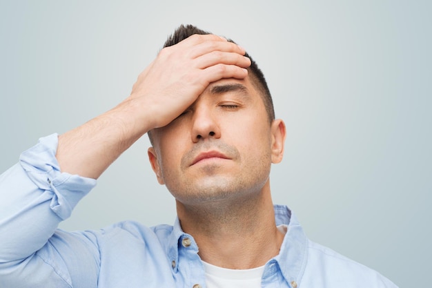 concept de stress, de maux de tête, de soins de santé et de personnes - homme malheureux aux yeux fermés touchant son front sur fond gris