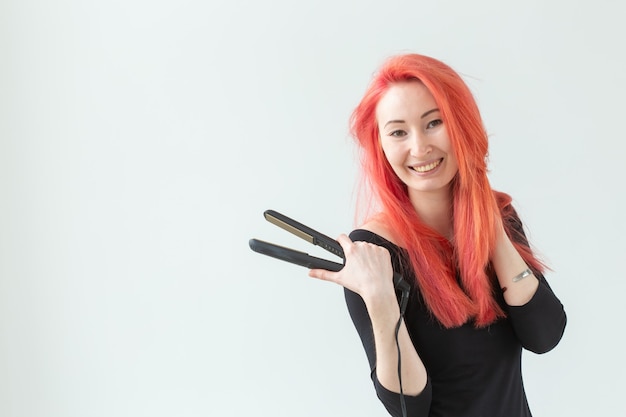 Concept de style, mode, coiffeur et personnes - élégante femme rousse avec fer à friser sur blanc