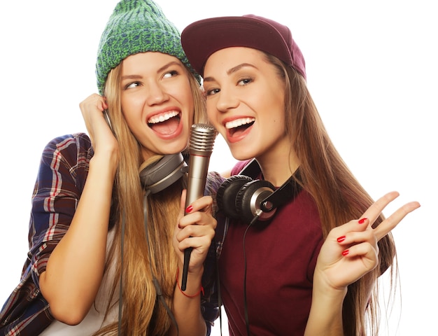 Concept de style de vie, de bonheur, d'émotion et de personnes : deux filles hipster de beauté avec un microphone chantant et s'amusant