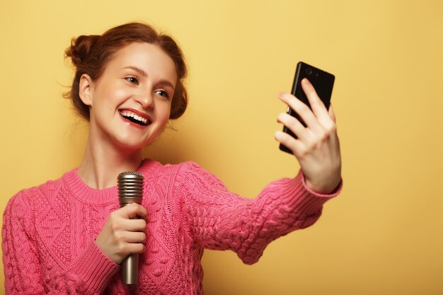 Concept de style de vie, de bonheur, d'émotion et de personnes. fille de beauté avec un microphone chantant et prenant selfie