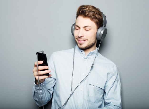 Concept de style de vie, de bonheur, d'émotion et de personnes: homme tenant un téléphone mobile et licté en musique sur un espace gris