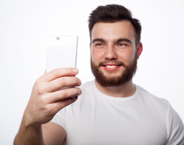 Concept de style de vie, de bonheur et de personnes : jeune homme barbu avec un téléphone portable à la main sur fond gris.