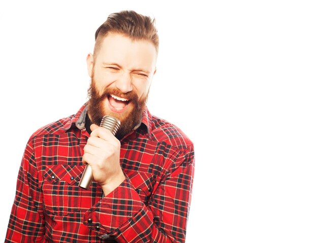 Concept de style de vie : un jeune homme avec une barbe portant une chemise blanche tenant un microphone et chantant. Style hippie. Sur fond blanc.